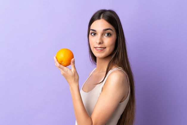 年轻人一位年轻的白人妇女 手拿橘子 被隔离在紫色的背景下饮食成人女人