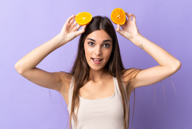食物一位年轻的白人妇女 手拿橘子 被隔离在紫色的背景下幽默健康营养