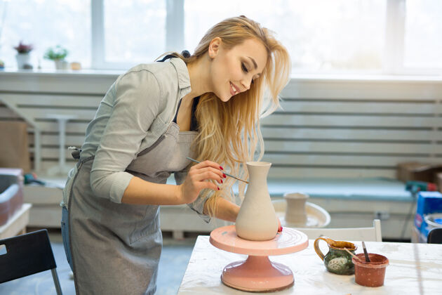 专业美丽的年轻女子在陶艺作坊里画陶罐技能材料微笑