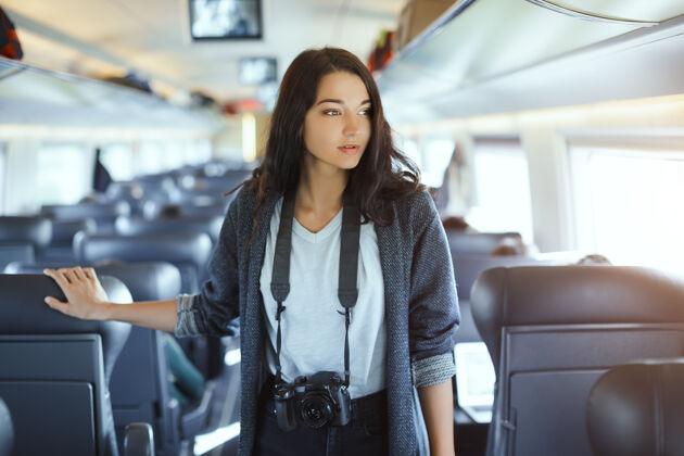乘客迷人的女摄影师和单反相机站在火车上 看着相机 而火车旅行混合
