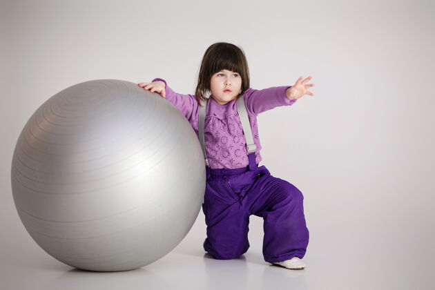 漂亮穿着紫色衣服的可爱小女孩 灰色背景上有一个健身用的大球无忧无虑精力充沛运动