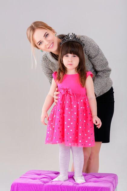 年轻美丽的小女孩穿着粉色公主裙 头戴皇冠 美丽的母亲在灰色背景下拥抱着美丽女孩母性