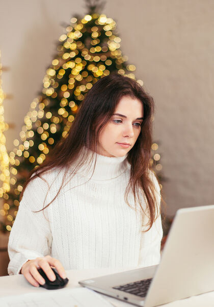书房一位黑发的年轻女子在家里用笔记本电脑遥控工作 背景是圣诞节的文件树喜庆的在家工作的氛围2021年冬季商务女性工作场所