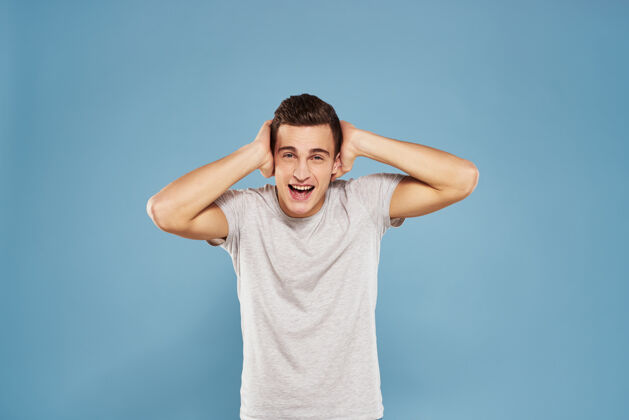 表演一个穿着白色t恤的快乐男人用手在蓝色的墙上做手势衬衫现代模特