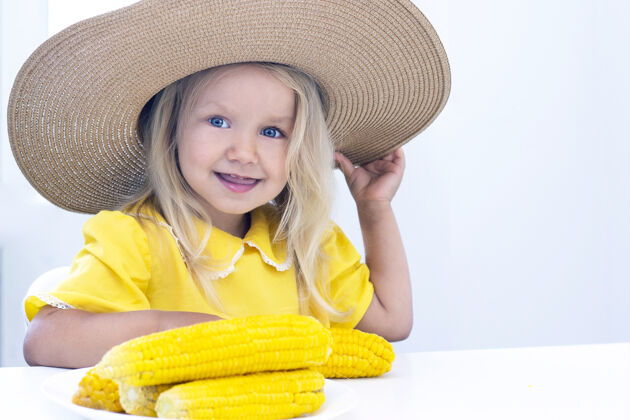 年轻穿着黄色衣服戴草帽的小女孩吃玉米 夏天照片.on背景光小小女人