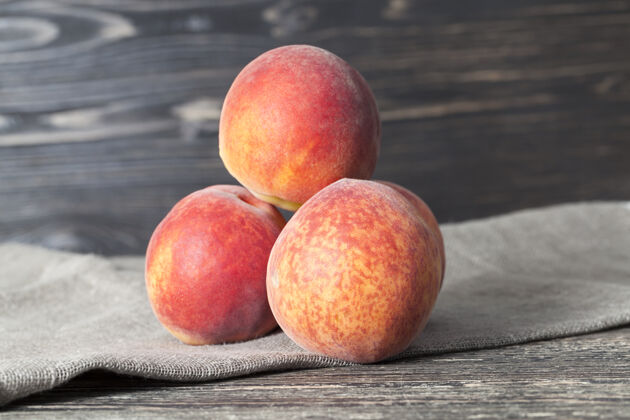 深色木桌上放着三个桃子和一张亚麻餐巾果肉叶季节