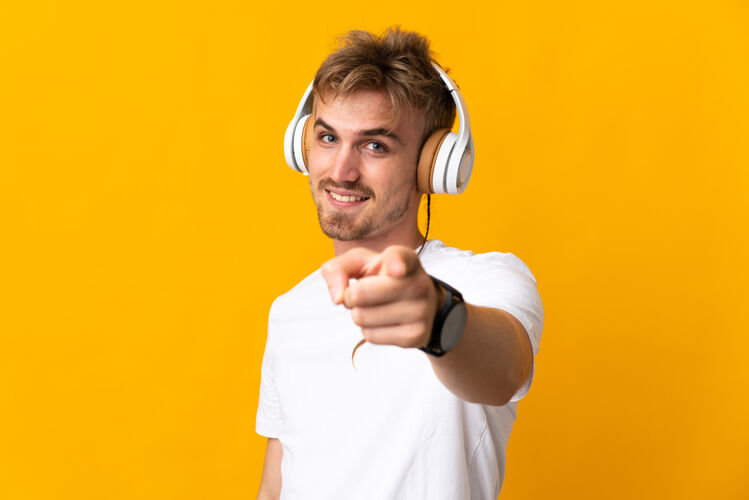 男年轻英俊的金发男人孤立在黄色听音乐 并指着前面巴德男人年轻