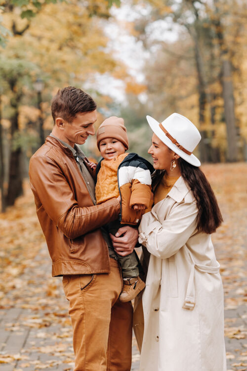 宝贝爸爸和妈妈带着儿子在秋天的公园里散步一家人在金秋的自然公园里散步母亲户外童年