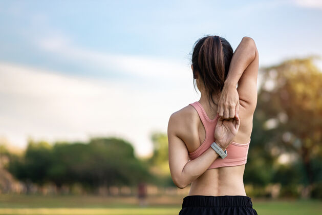 拉伸穿着粉色运动服的年轻成年女性在公园户外伸展肌肉 运动女性热身准备跑步和慢跑早上好健康 健身 运动和工作生活平衡概念训练健康年轻