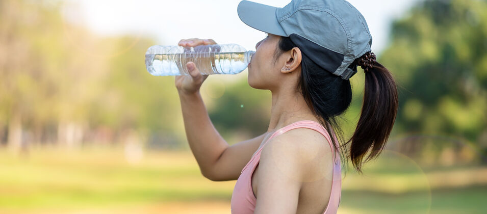 公园年轻的健身女士在公园户外伸展肌肉时饮用能量水 亚洲运动员在公园跑步锻炼早上好运动健康理念身体散步锻炼