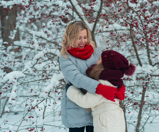 户外微笑的年轻妈妈和她可爱的女儿手拉着手一起滑冰树可爱雪