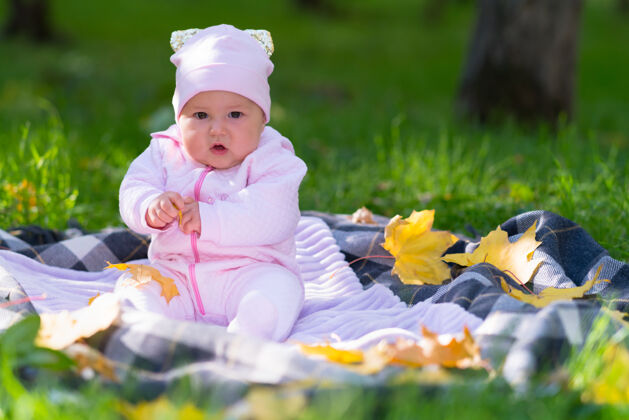 分散公园里 一个穿着粉红色衣服的婴儿在秋叶间的野餐地毯上玩耍肖像秋天草地