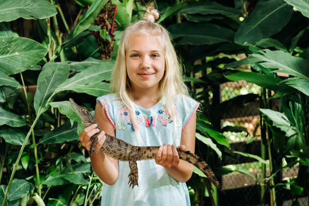 动物园毛里求斯岛上一个快乐的小女孩的夏日肖像画鳄鱼女孩在动物园里抱着一条鳄鱼家庭小女孩童年