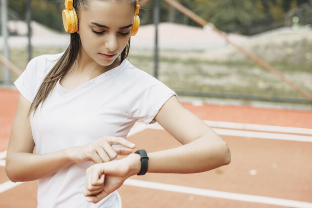 深色一位迷人的年轻女性一边听音乐一边在跑步前摆好运动手表的画像草地冠军跑步