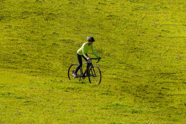 自行车一个年轻的微笑着的女孩骑着自行车从绿色明亮的草地上滑下山坡活跃山针叶树
