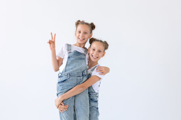 漂亮家庭和爱的概念-两个微笑的双胞胎姐妹拥抱在白色的表面活跃享受快乐