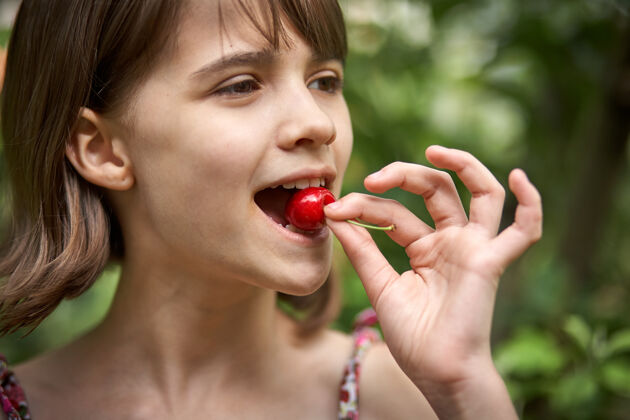 美丽在花园里笑着吃樱桃的小女孩的画像户外笑肖像
