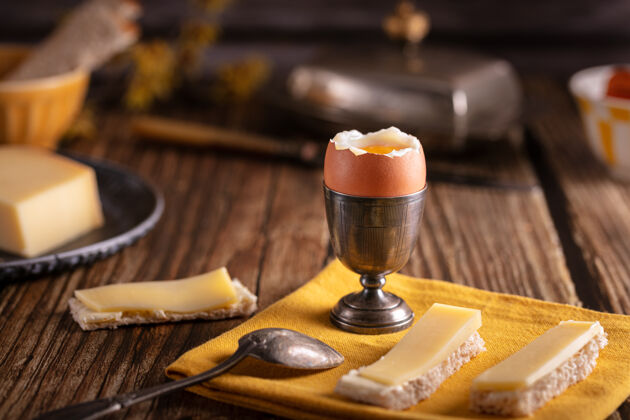 美味木桌上放着煮鸡蛋的银蛋杯 还有面包和奶酪法国烹饪葡萄酒