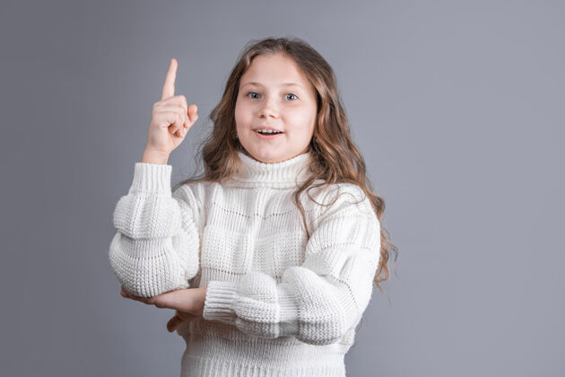 快乐一个年轻漂亮的金发小女孩的肖像 穿着白色毛衣 微笑着 手指向上 是文本的理想场所教育可爱手指