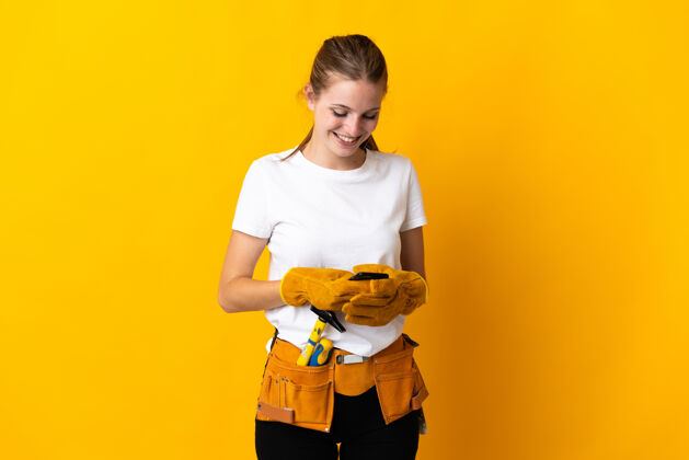 工匠被隔离在黄色背景上的年轻电工用手机发信息电话女性手机