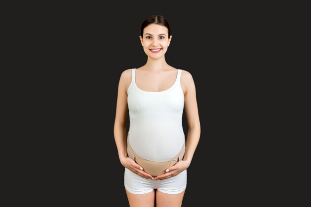 母亲特写镜头中的孕妇穿着内衣 用弹性妊娠绷带使疼痛消失在黄色的背景上空间矫形外科腹部支撑带概念绷带肖像身体