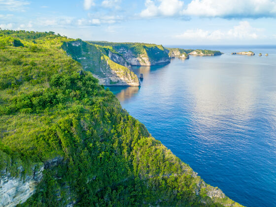 巴厘岛印度尼西亚海岸在岛上佩尼达丛林上岩石 云蓝色的天空.天线查看旅游海岸线海岸