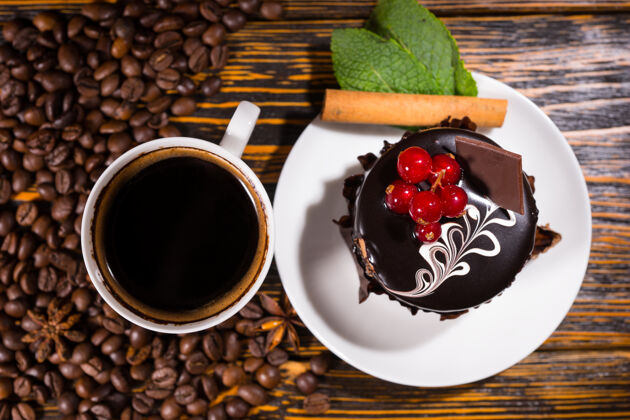 杯子俯瞰图咖啡豆旁边的白色马克杯和甜点装饰着巧克力和红色浆果的木桌上水果特写顶部