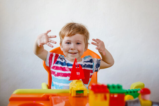 活动一个欢笑的小男孩坐在桌子旁 手里拿着五颜六色的玩具向上向上高质量的照片细节创意欢笑