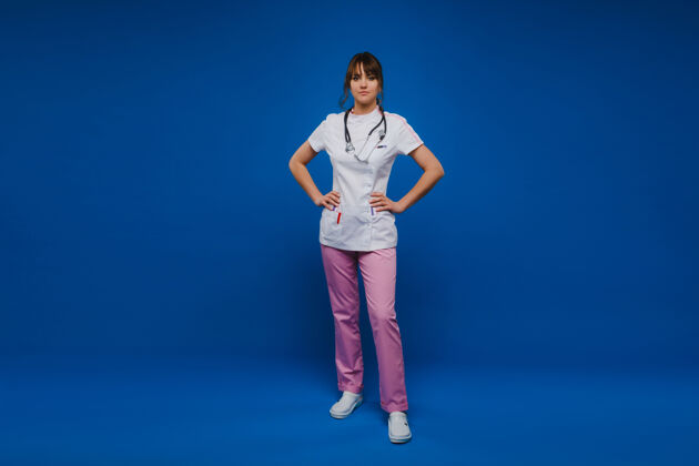 年轻年轻的女医生用听诊器隔离在蓝色背景上诊所室内自信