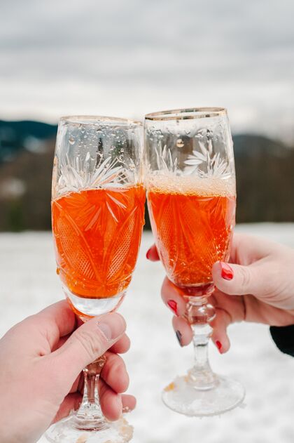 酒在冬山的背景下 男人和女人手拿一个两杯香槟冬天人庆祝