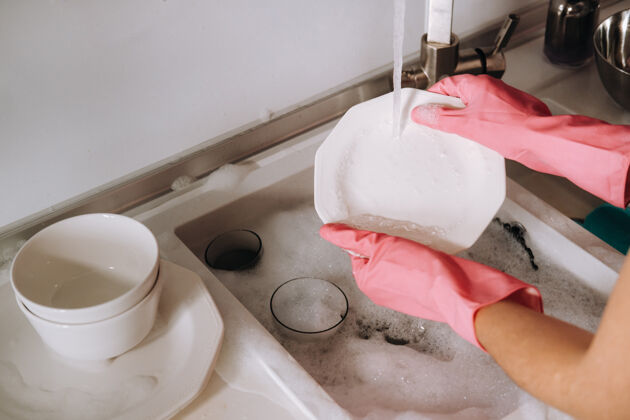 洗衣粉一个戴着粉色手套的家庭主妇在水槽里用手洗盘子清洁剂女孩在家里戴着手套洗碗室内洗衣机女士