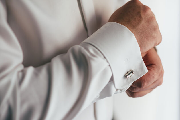 正式男手放在一件白色衬衫的表面 袖子上有袖扣和手表 拍下了特写镜头紧固件零件纺织品