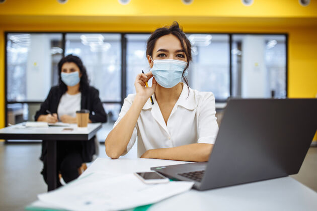 社会距离一位妇女在办公桌上用笔记本电脑工作 戴着医用口罩 在covid-19大流行期间保持安全成长护理女人