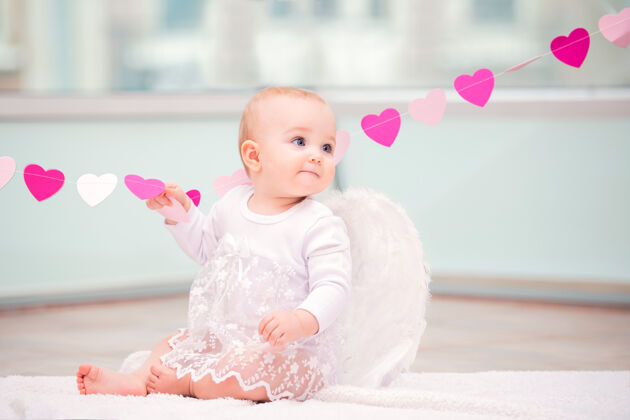宝贝一个活泼淘气的婴儿的肖像 白色天使的翅膀触动着一个心形饰物穿天使花环