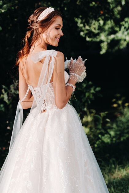 手套一个优雅的新娘在一个自然公园里穿着白色的裙子和一束花束的肖像花艺可爱新娘