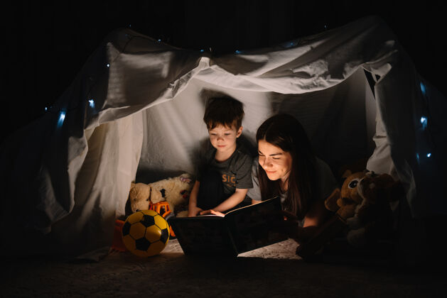 父母幸福家庭母子俩在帐篷里用手电筒看书主页.家庭概念地板成人童话