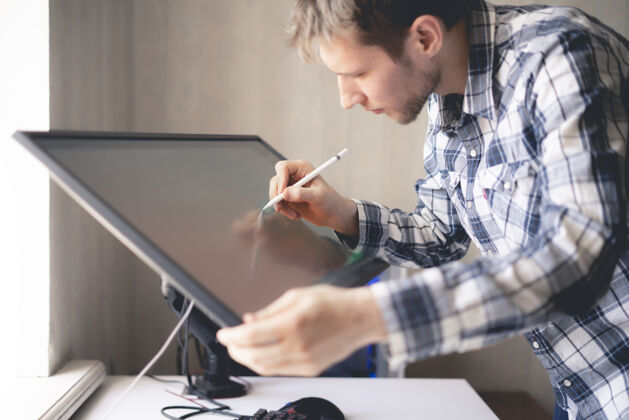 办公室一位年轻的男性数码艺术家在工作室的电脑屏幕上画画计算机工具绘图
