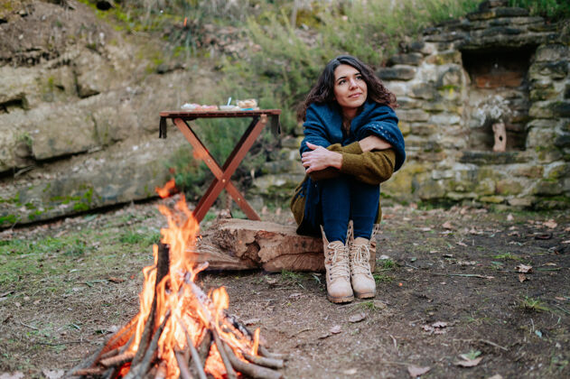 一起冬日野餐时坐在火炉旁的年轻女子温暖夜晚森林