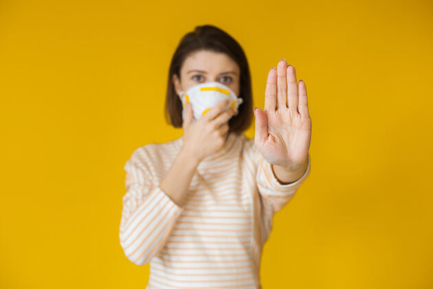 空气一个戴着白色面具的白种女人在黄色的墙上摆姿势 示意停车标志暴发新颖担心