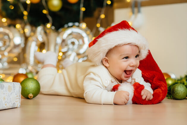 灯可爱的微笑的宝宝躺在圣诞树下玩礼物新温暖宝贝