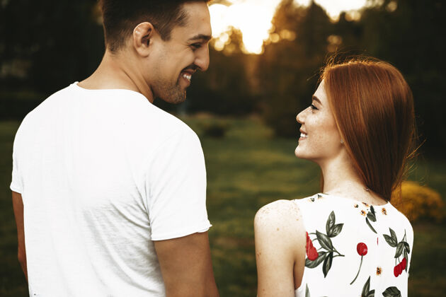 爱一对迷人的情侣手牵着手 看着对方笑着对着夕阳 同时在外面约会家庭红发拥抱