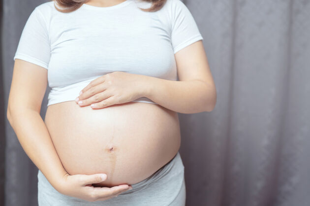 产前新妈妈穿着白色内衣的孕妇用手抚摸肚子和宝宝等待房子怀孕