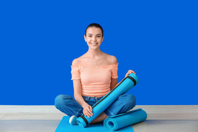 垫子穿着瑜伽垫坐在彩色墙旁边的年轻女子瑜伽女人健康