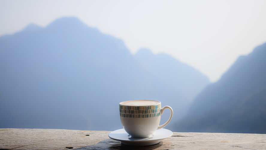 山热咖啡卡布奇诺在木制露台上的白色杯子与美丽的风景自然背景的薄雾晨曦山在phaheedoi清莱泰国咖啡雾咖啡杯