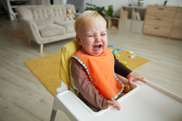 学习男婴坐在婴儿椅上 在房间里哭吃休闲服家庭内部