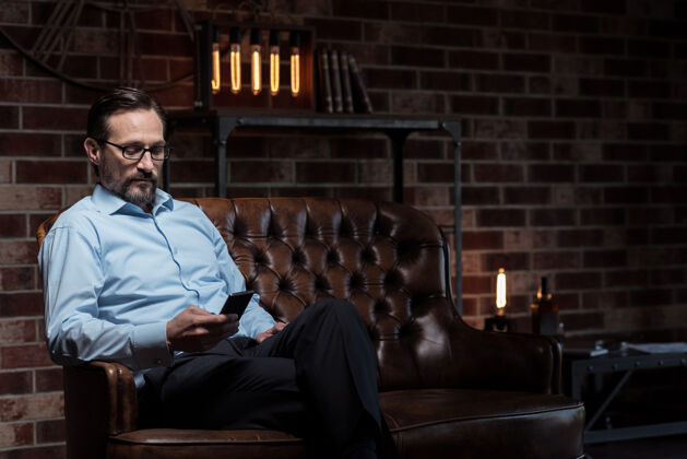 创新现代电子设备帅哥努力工作的成年男子交叉双腿 坐在沙发上看手机书房沙发十字架