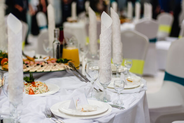 招待会餐厅里摆着白色喜庆的桌子 上面摆着为晚餐准备的玻璃杯和盘子桌布婚礼服务