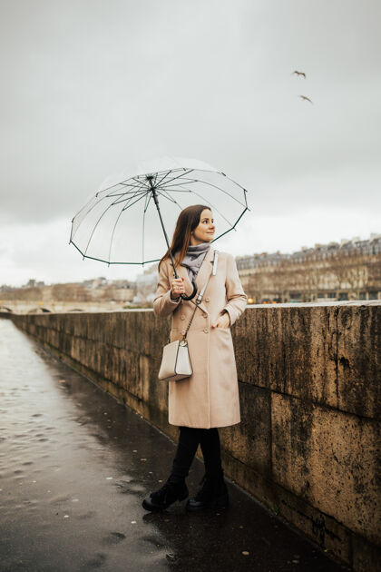 古老时尚的女孩带着透明的雨伞在城市中俯瞰 风景带着模特在雨天地标城市河流