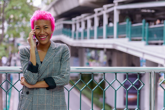 个人年轻叛逆的亚洲女商人的肖像 粉红色的头发在城市户外的人行天桥上20多岁朋克连接