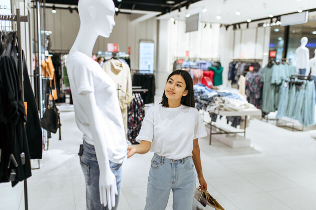 消费主义快乐的女人站在人体模特面前 穿着衣服女店员在时装精品店购物的人 购物狂 看服装的购物者购物者女孩选择